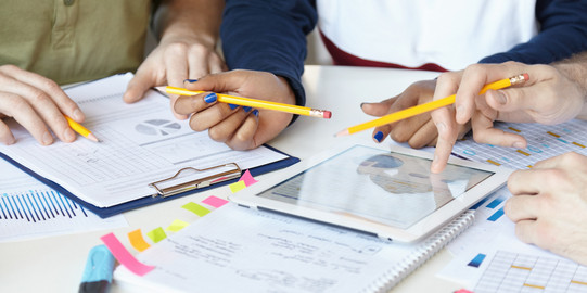 Diagramme_03 Auf einem Tisch liegen Blöcke und Blätter, ein Tablett, welches von einer Hand benutzt wird.
